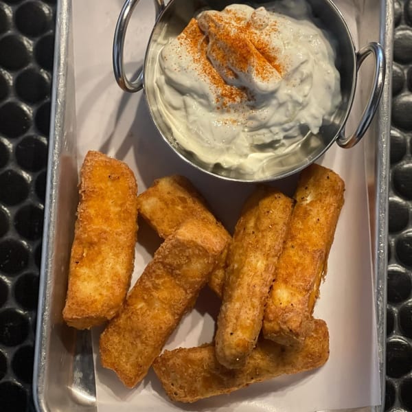 Fried halloumi cheese sticks with a side of tzatziki sauce, sprinkled with paprika.