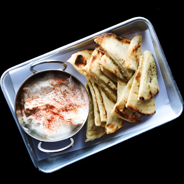 Tzatziki dip with paprika in a metal bowl, served with grilled pita bread on a tray.