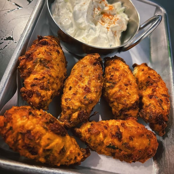 Six golden-brown fried Greek fritters, likely zucchini or cheese, with a side of tzatziki sauce.