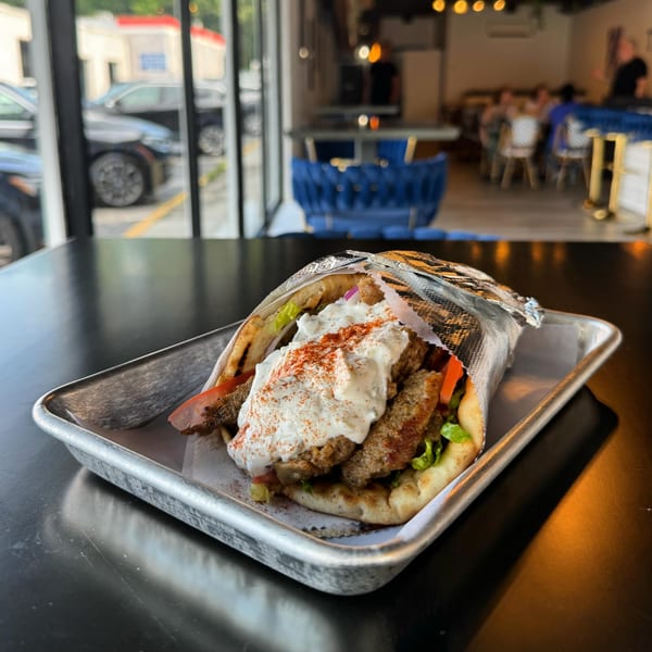 A Twisted Greek gyro with meat, tzatziki, and paprika on a metal tray inside the restaurant.