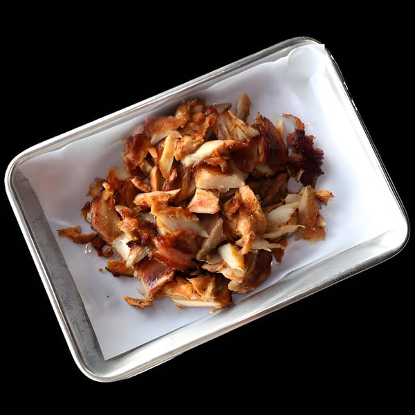 Close-up of a metal tray filled with golden-brown, chopped chicken shawarma on white parchment paper.